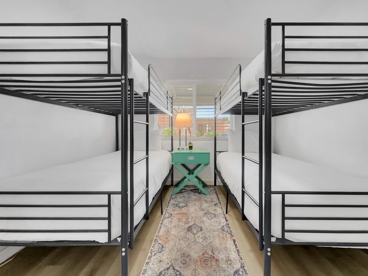 This image features a set of bunk beds with a green side table and a lamp, set on a decorative rug. The playful and relaxed mood, along with the cozy atmosphere, suggests a space where friends can bond, share late-night chats, and reflect on their downtown adventures together.