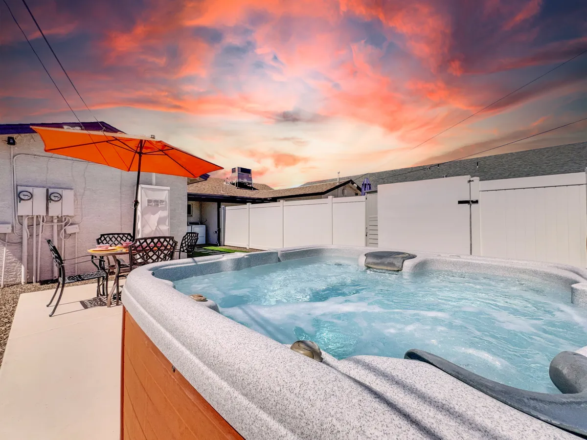 This exterior image highlights a private hot tub positioned under an orange umbrella, surrounded by an inviting outdoor seating area. The tranquil setting is complemented by soft, sunset lighting, creating a romantic and serene ambiance.
