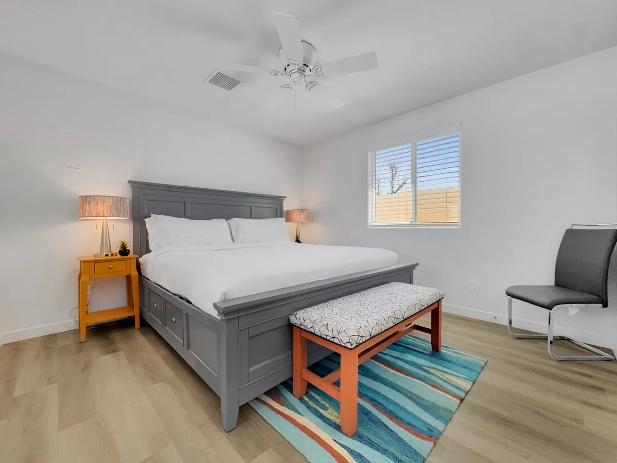 A cozy bedroom scene with a well-made bed, nightstand, decorative bench at the foot, and a soft rug underfoot. The room is well-lit with natural light, creating a welcoming and relaxing environment ideal for reading, resting, or unwinding after a busy day.