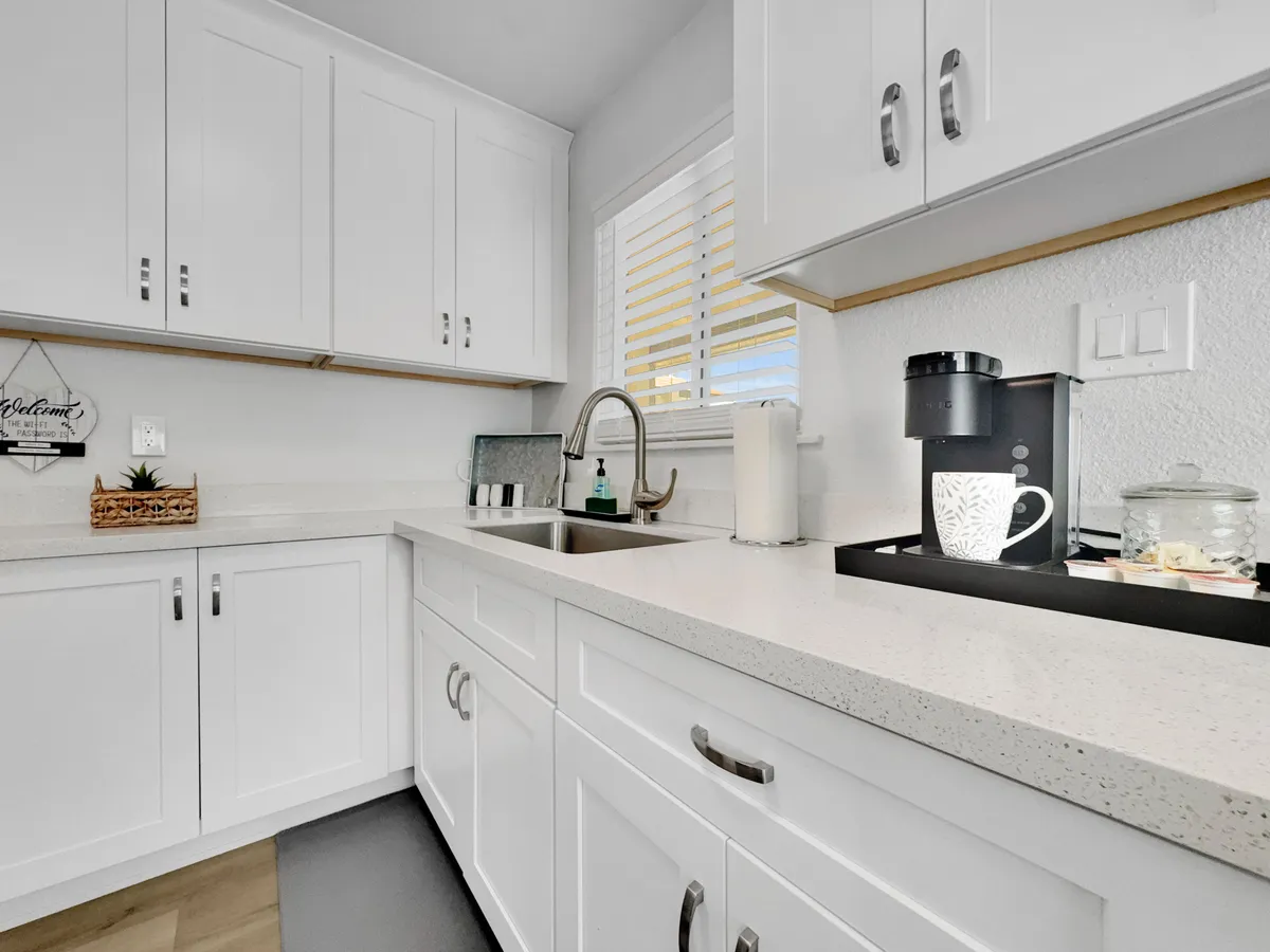 Clean white cabinetry surrounds a modern coffee maker and decorative dishware, creating an atmosphere that's both functional and welcoming. The image evokes the ritual of morning coffee and meal preparation.