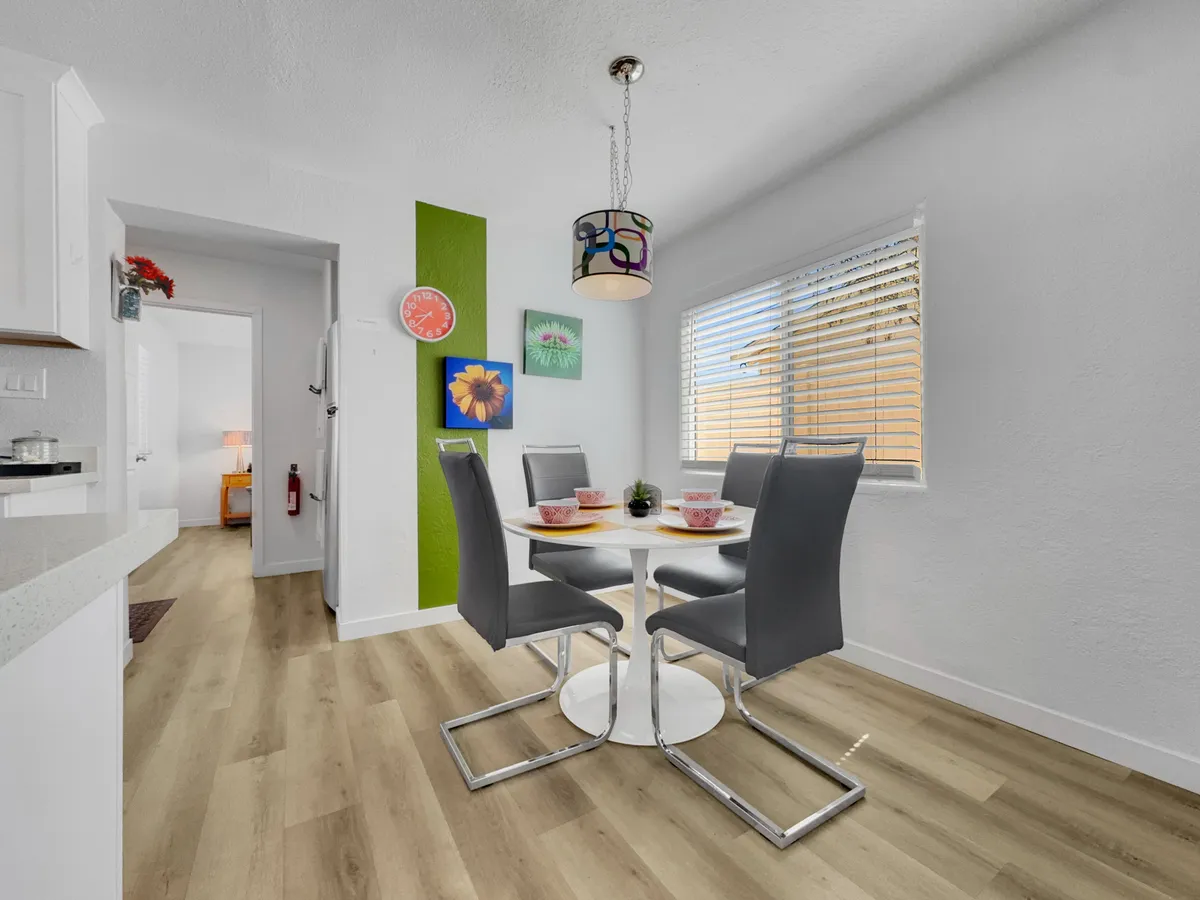 A warm and welcoming dining area is shown, featuring a central dining table, colorful wall art, and a distinctive lighting fixture. The space is ideal for casual gatherings or enjoying a coffee before heading out for a morning walk.